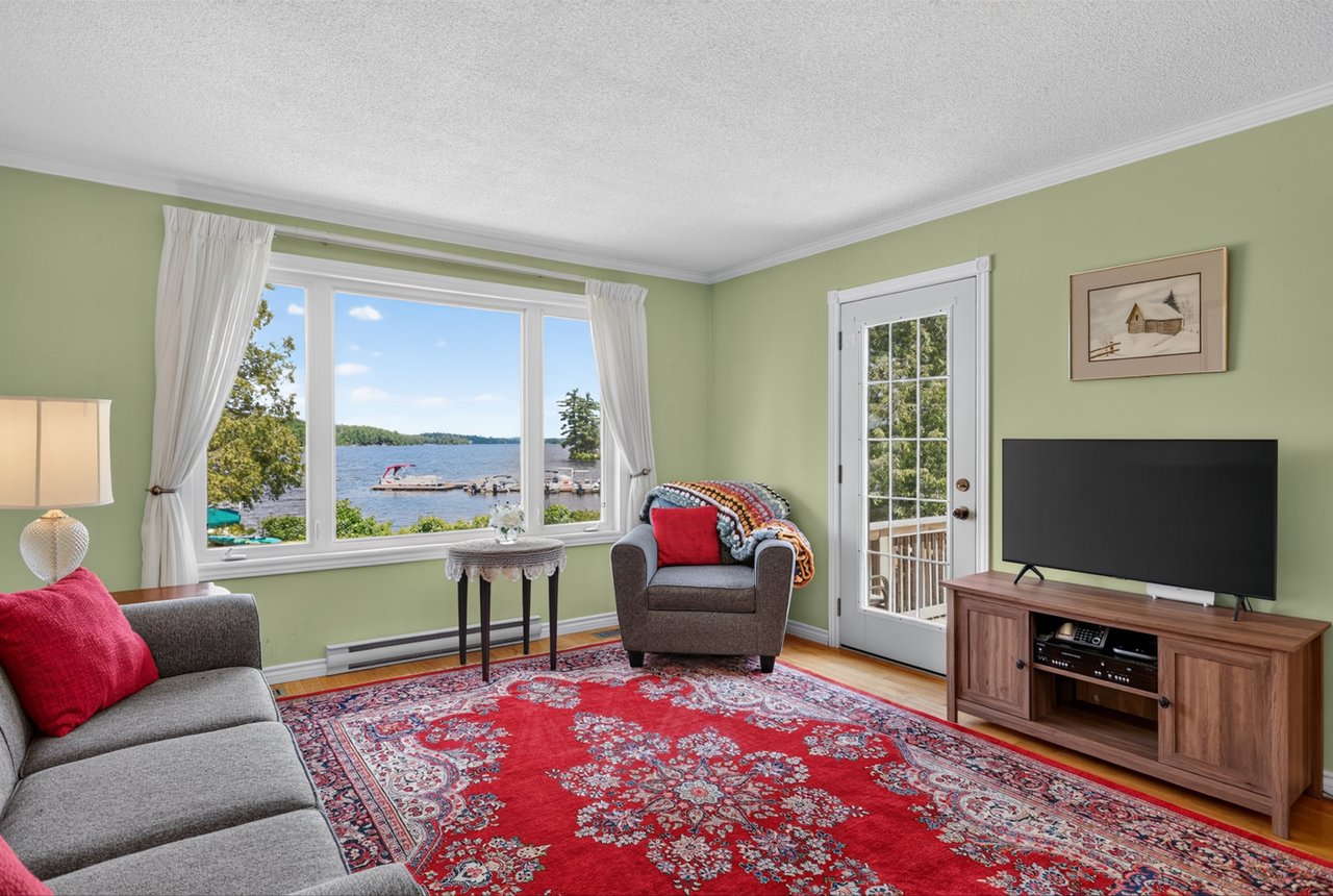 Living room with a red patterned rug and large windows overlooking a lake and dock.
