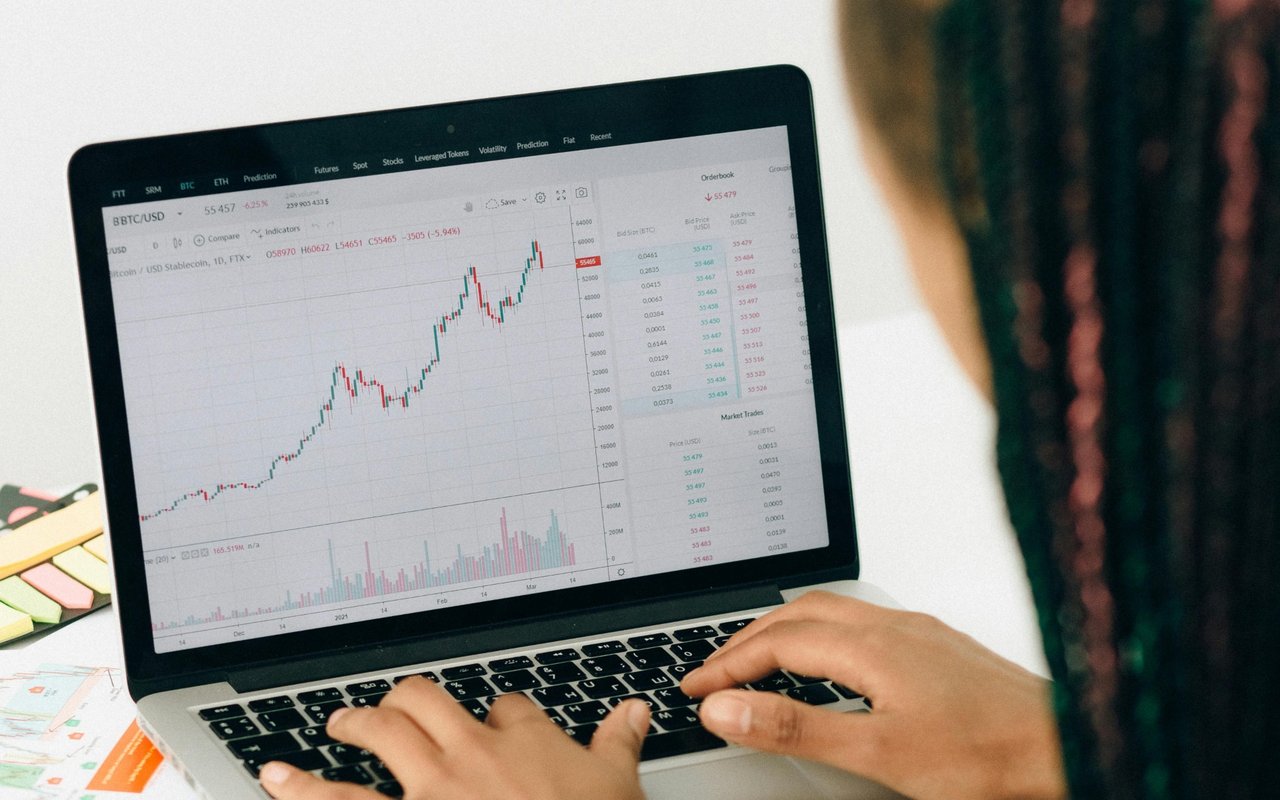 Hands type on a laptop displaying a rising cryptocurrency trading chart.
