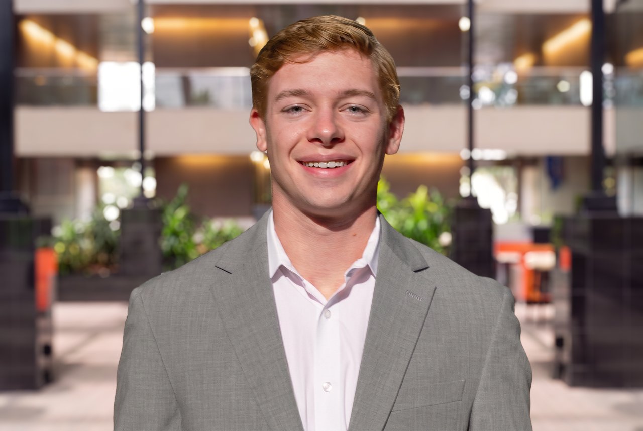 Liam Whitley in a gray suit jacket and white shirt in an office lobby.