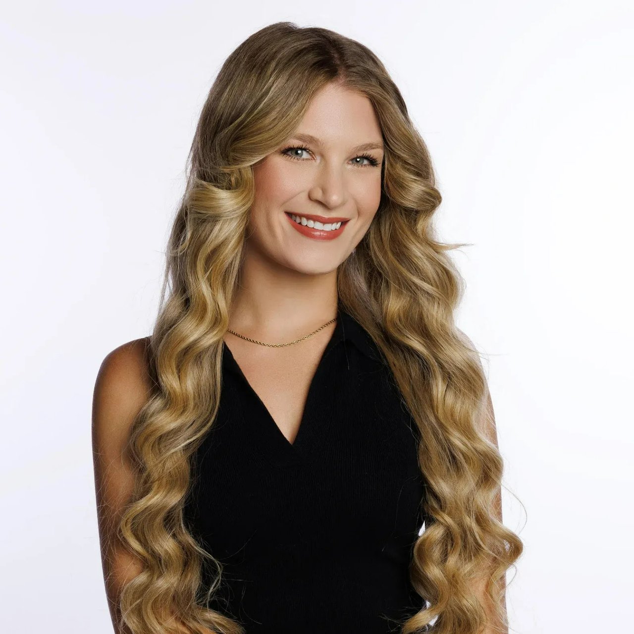 Kara McKenzie smiling in a black sleeveless top, with long wavy blonde hair.