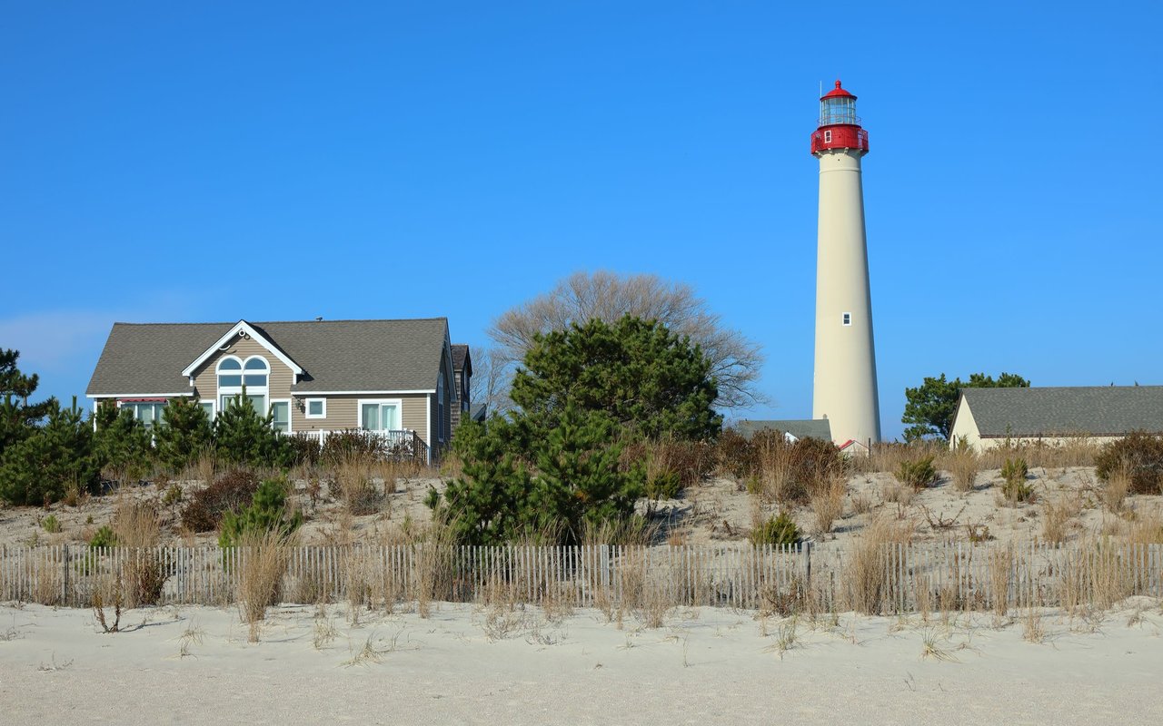 Cape May lighthouse and beach houses behind sandy dunes.