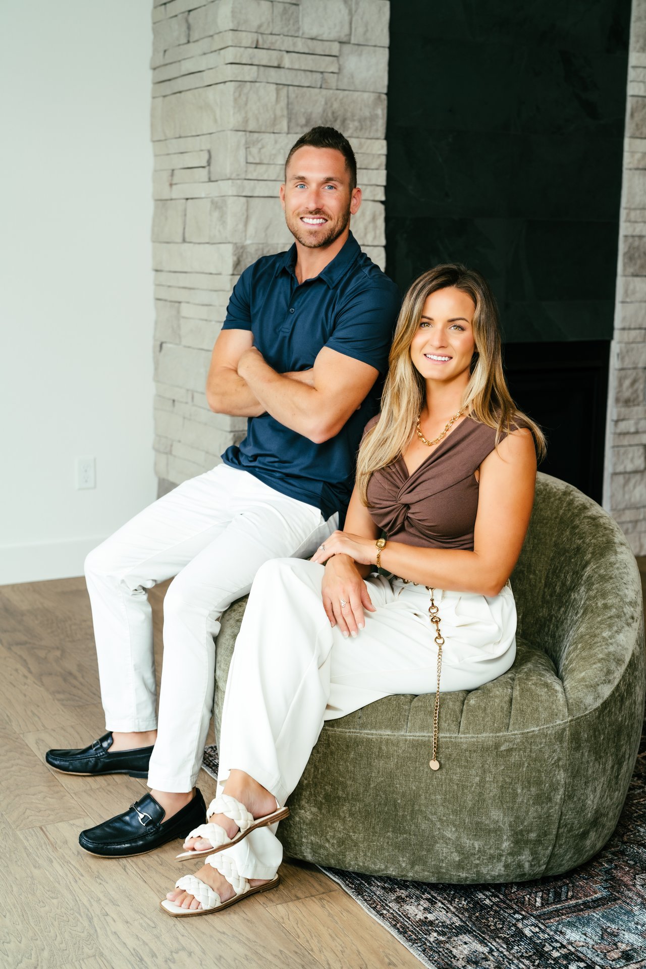 Andrew and Emily pose together indoors beside a pale stone fireplace.