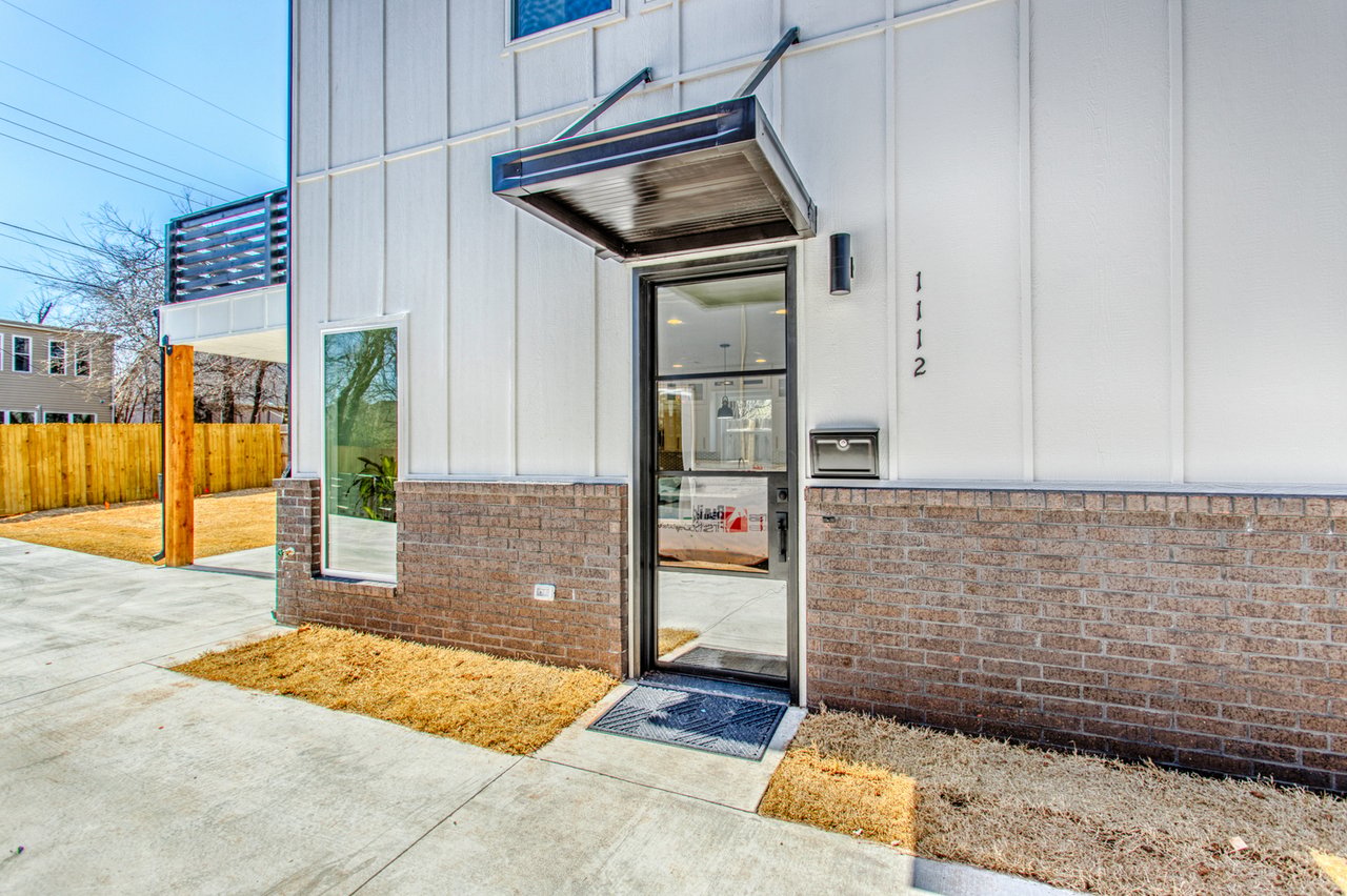 Front entrance with glass door, metal awning, and white siding over a brick base.
