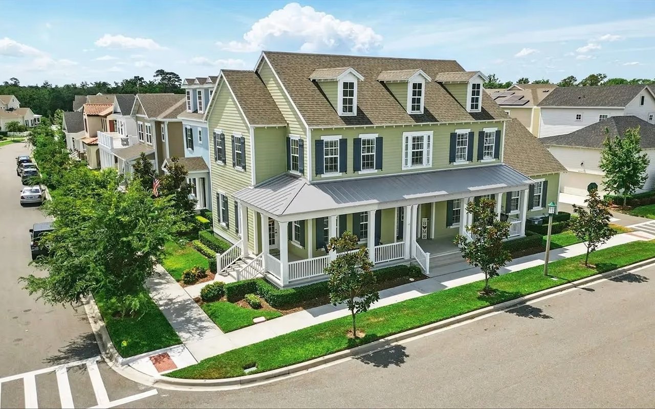 Pale green corner house in Celebration with a deep porch, white railings, and dark shutters.