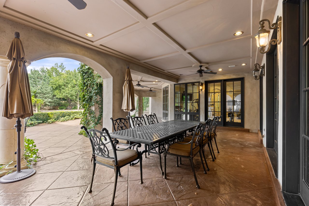 Covered stone patio with a long black dining table, arched openings, and garden views.