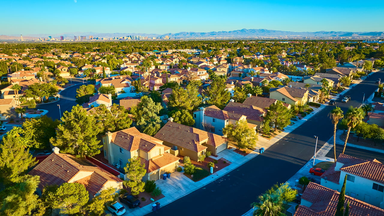 Aerial view of a residential community with tile-roof homes, palm trees, and distant mountains.