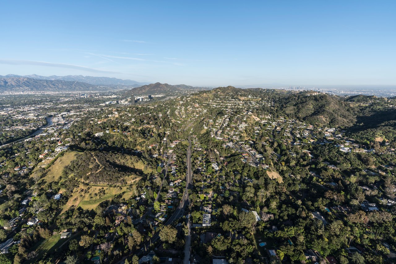 Aerial view of homes across green hills, with mountains and a distant city skyline.