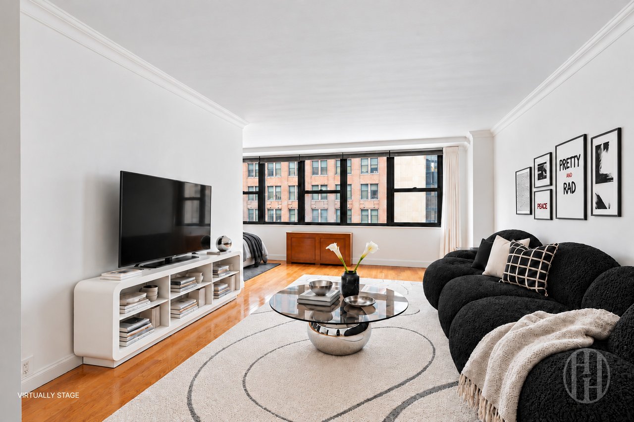 Virtually staged living room with wide windows, hardwood floors, and a black sectional.