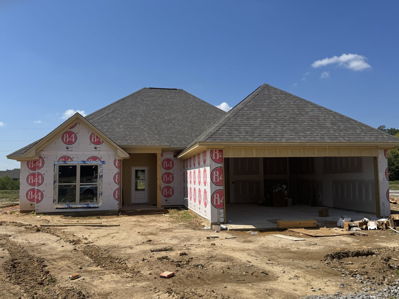 Single-story house under construction with an attached garage and unfinished, wrapped exterior walls.