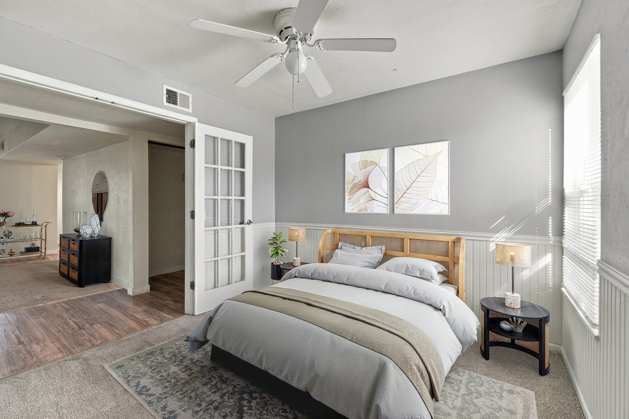 Staged bedroom with a wood-framed bed, ceiling fan, and open French door.