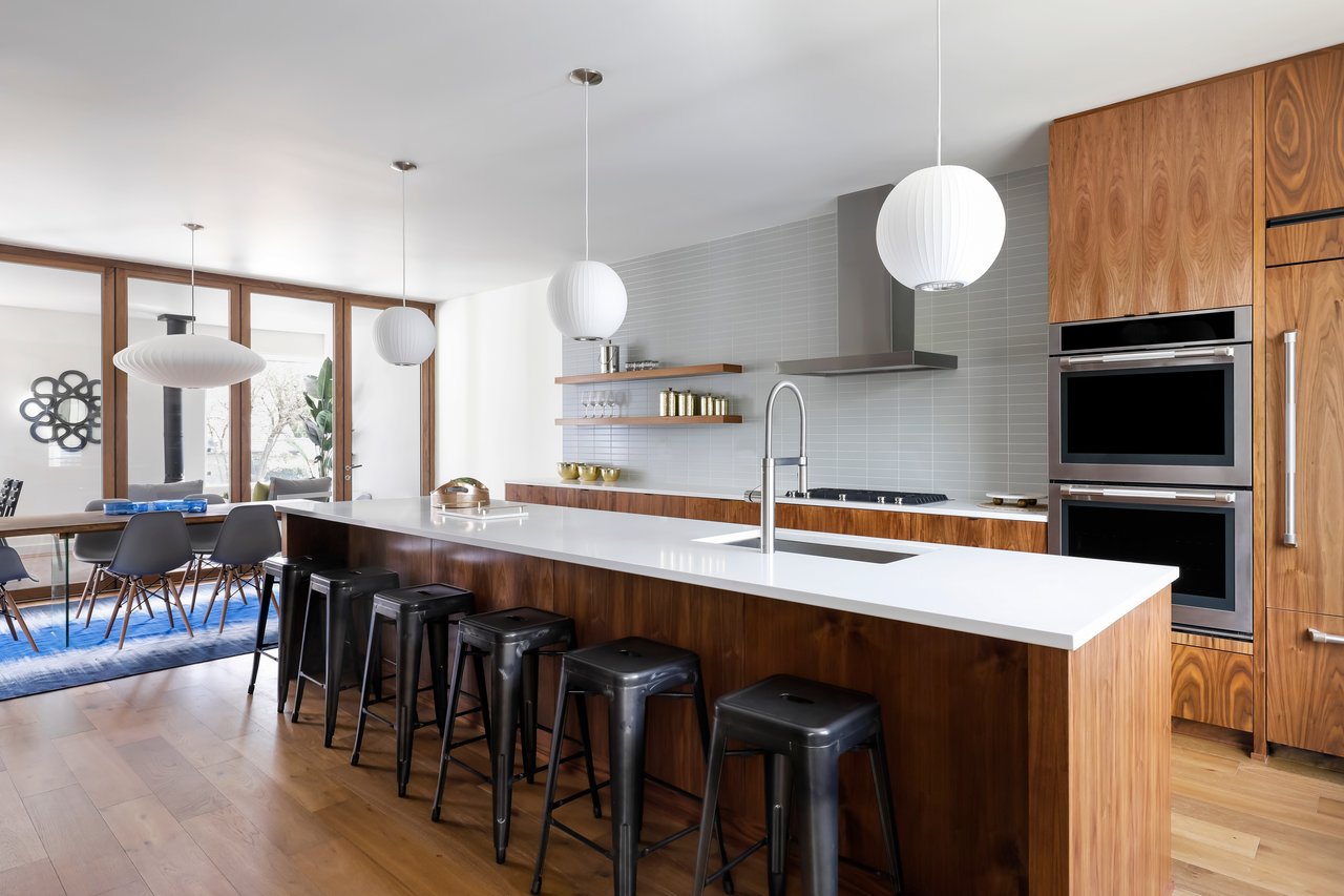 Modern kitchen with a long white island, wood cabinetry, and pendant lights.