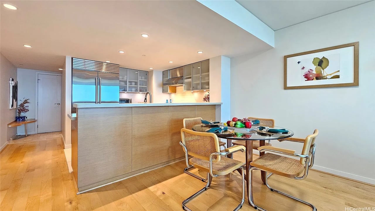Open kitchen and dining area with a wood-front island and round glass table with woven chairs.