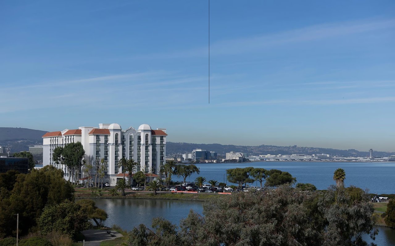 Waterfront building beside a bay, with a lagoon and tree-lined grounds in the foreground.