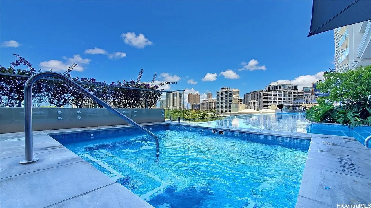 Outdoor swimming pool overlooking a city skyline, with a tiled deck and metal handrail.
