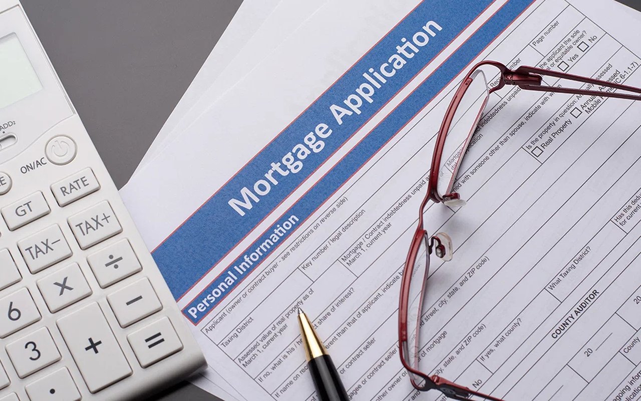 Mortgage application form beside a calculator, red eyeglasses, and a pen.