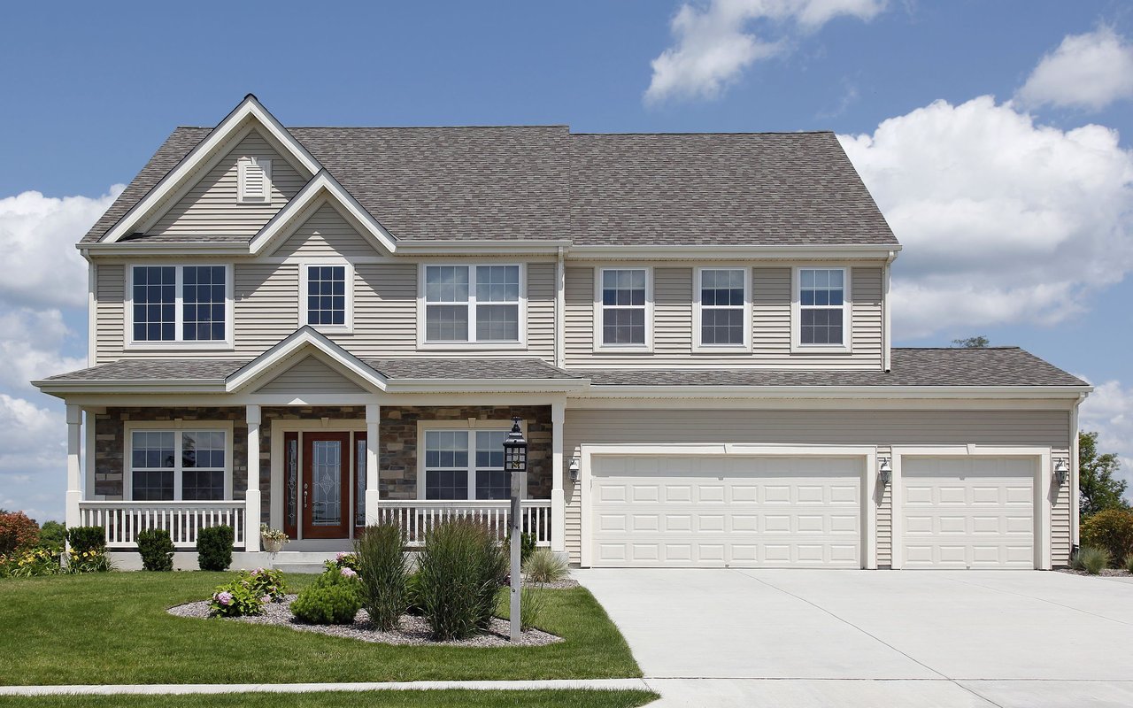 Two-story gray home with a covered porch, stone accents, and a three-car garage.