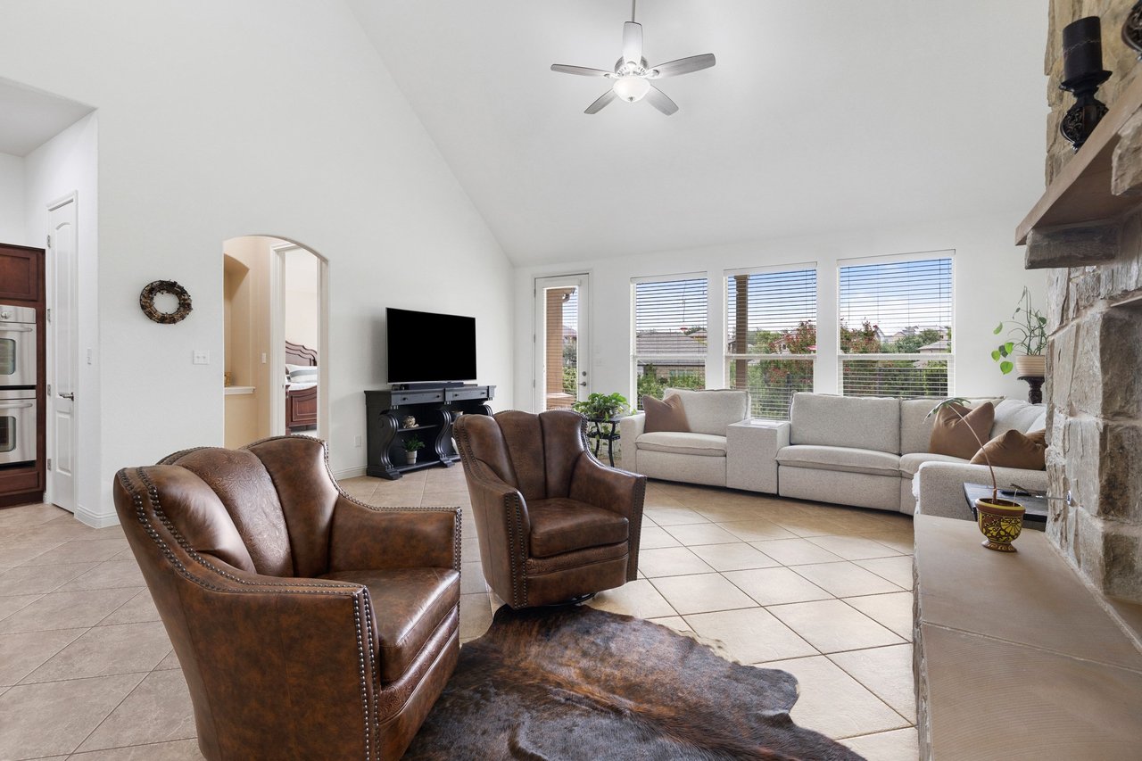Furnished living room with a vaulted ceiling, cream sectional, leather chairs, and stone fireplace.
