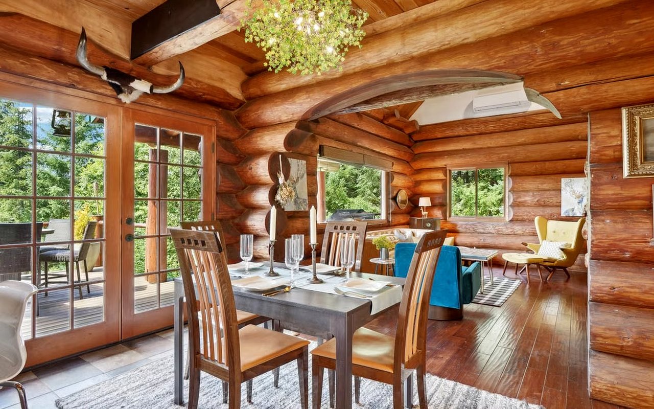 Log home dining and living area with exposed timber beams and glass doors opening to a deck.