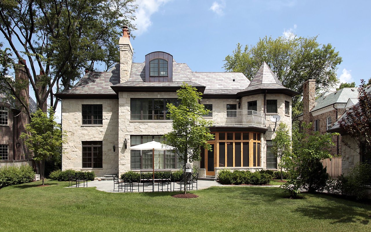 Stone house with a turret and balcony overlooking a lawn and furnished patio.