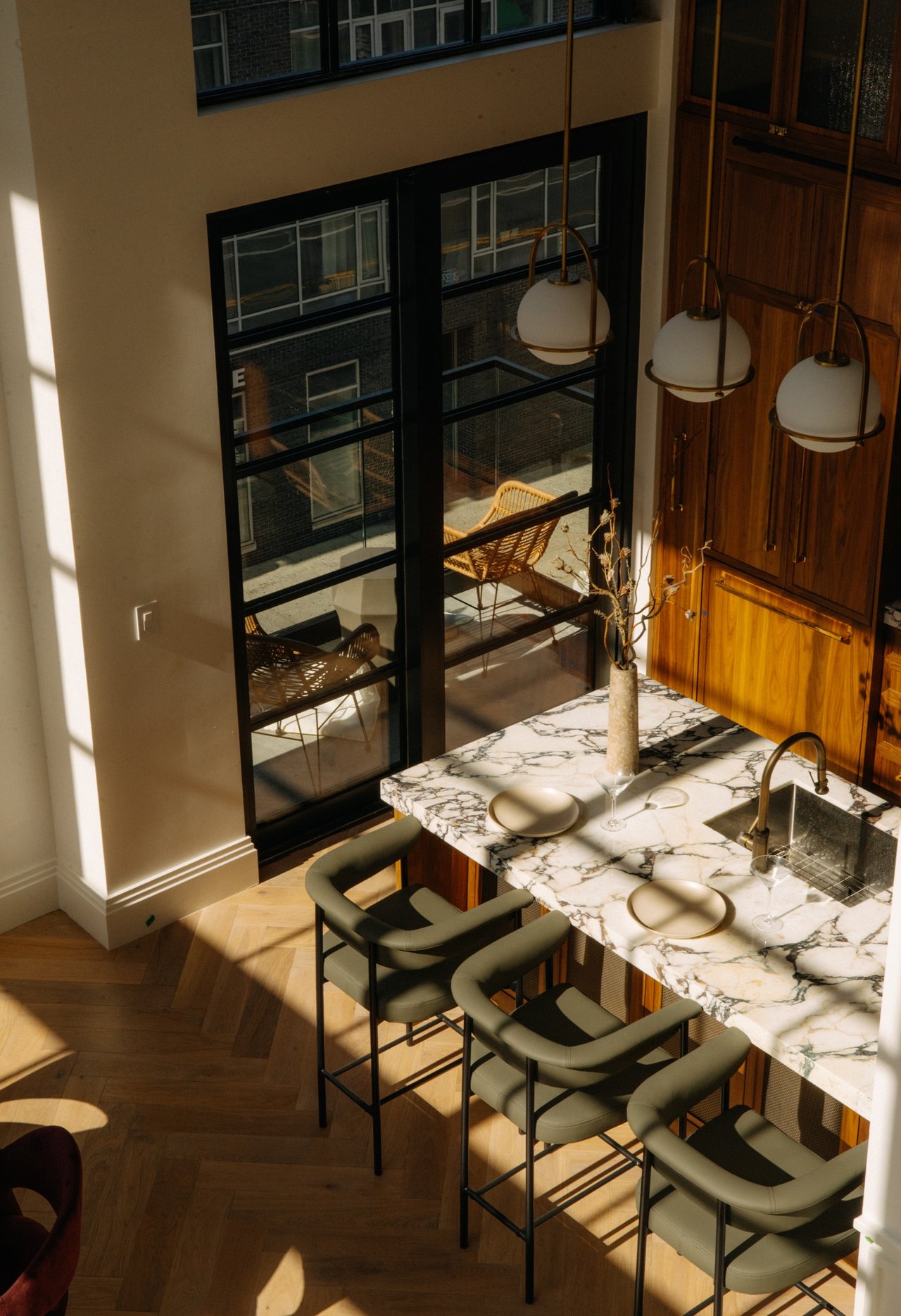 Kitchen with a veined marble island, green bar stools, wood cabinetry, and tall black-framed windows.