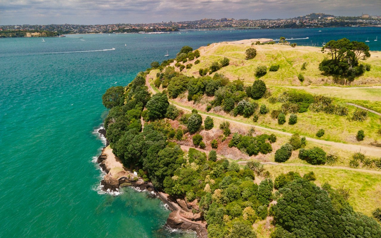 Aerial view of a green headland beside turquoise water, with winding paths and boats.