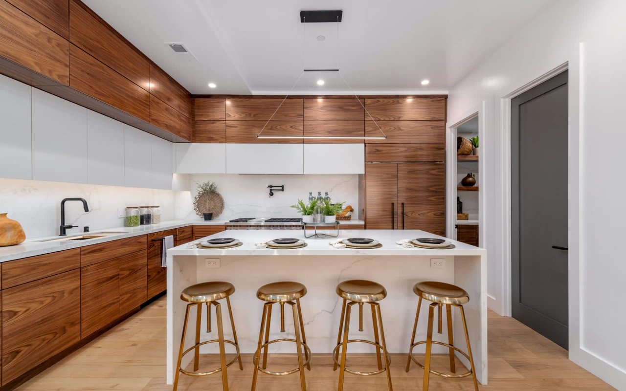 Modern kitchen with walnut cabinetry, a marble island, and four brass stools.