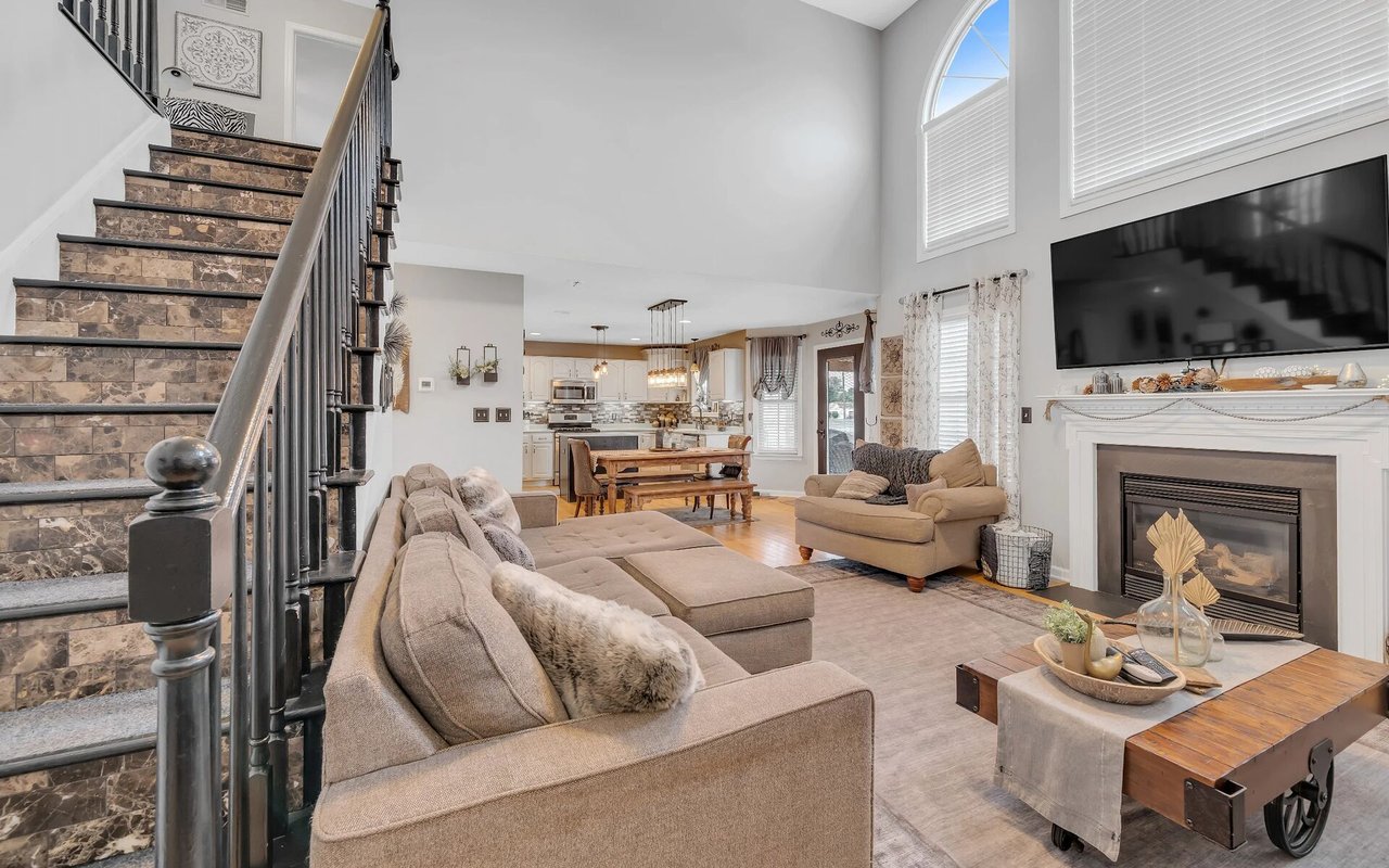Living room with a stone staircase, fireplace, tall windows, and adjoining kitchen.