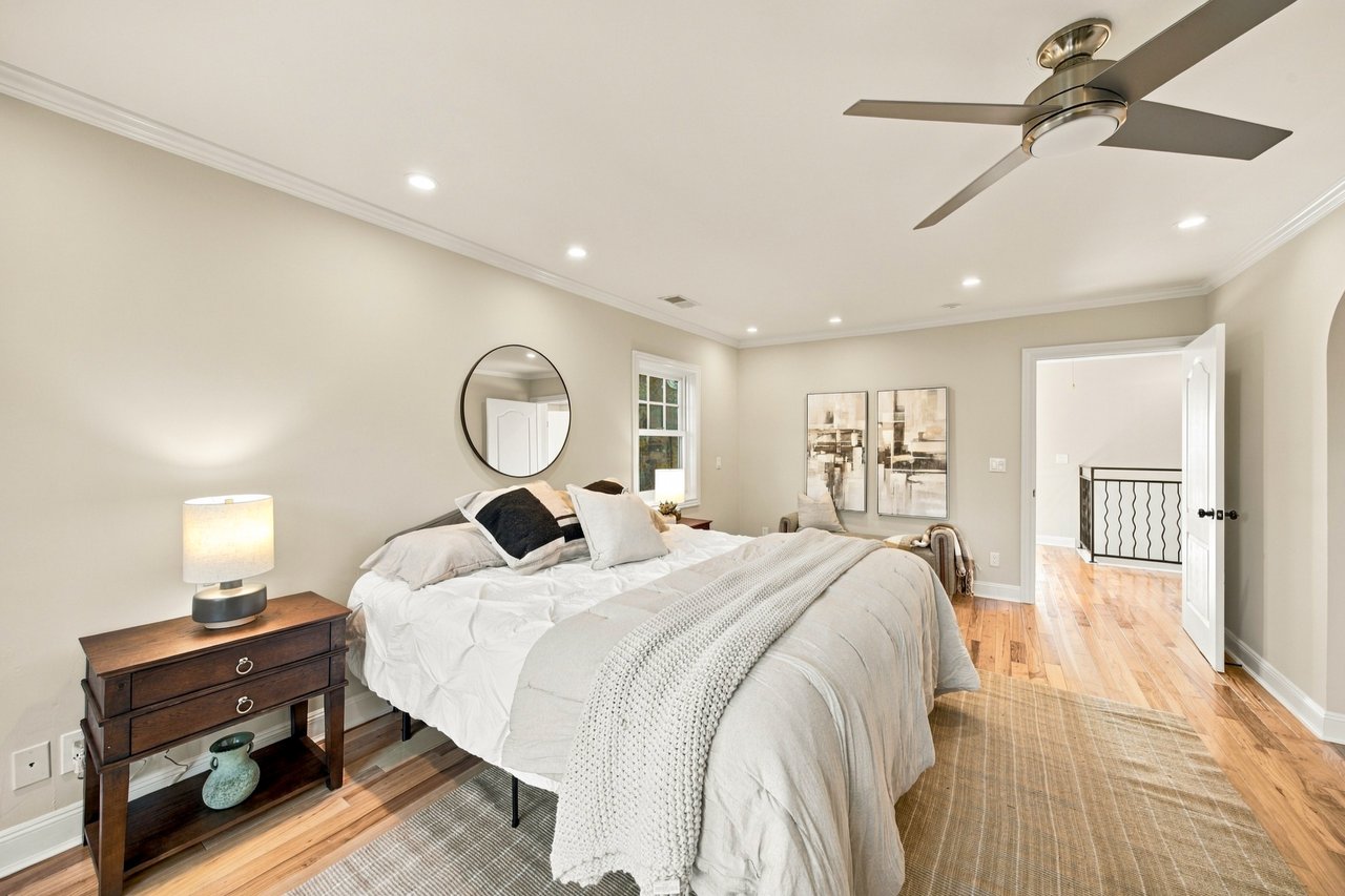 Staged bedroom with white bedding, a dark wood nightstand, and a ceiling fan.