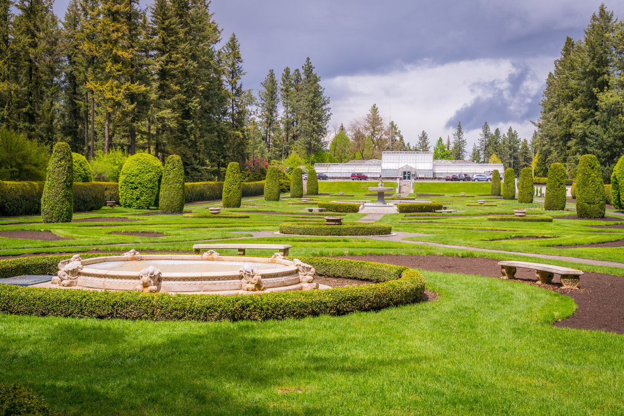 Formal garden with clipped hedges, a stone fountain, and a glass greenhouse.
