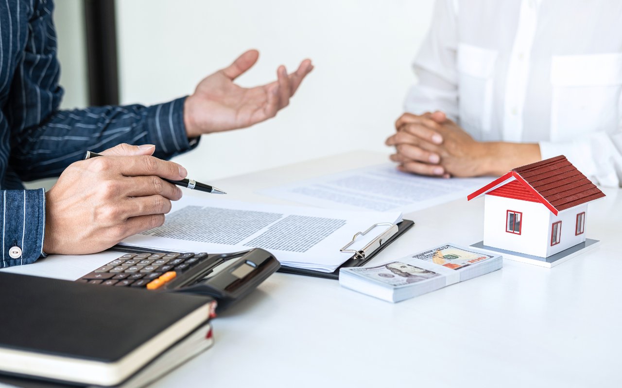 People review home pricing documents beside a calculator and model house.