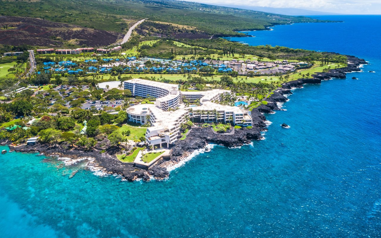 Aerial view of a coastal resort beside turquoise water and a rugged shoreline.
