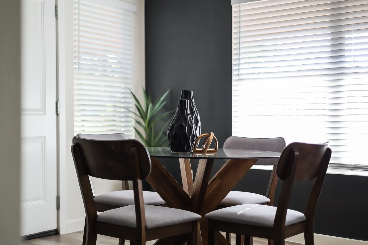 Dining area with a glass-top table, upholstered chairs, and a dark accent wall.