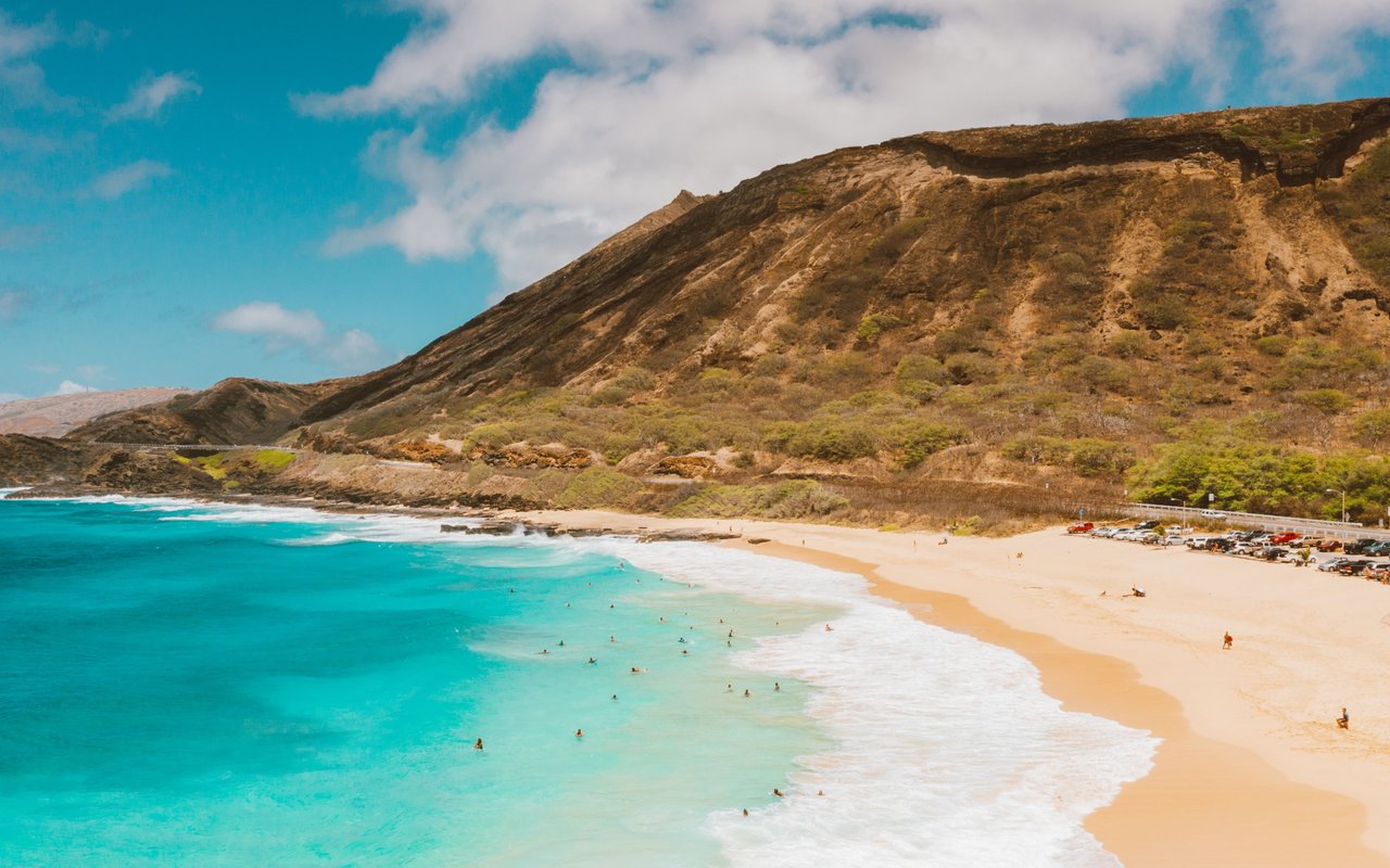 Turquoise waves wash onto a sandy beach beneath a dry, rugged headland.