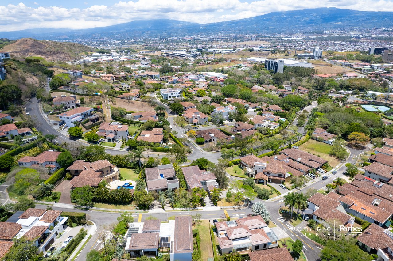 Aerial view of a suburban neighborhood with red-tile roofs, green hills, and mountains beyond.