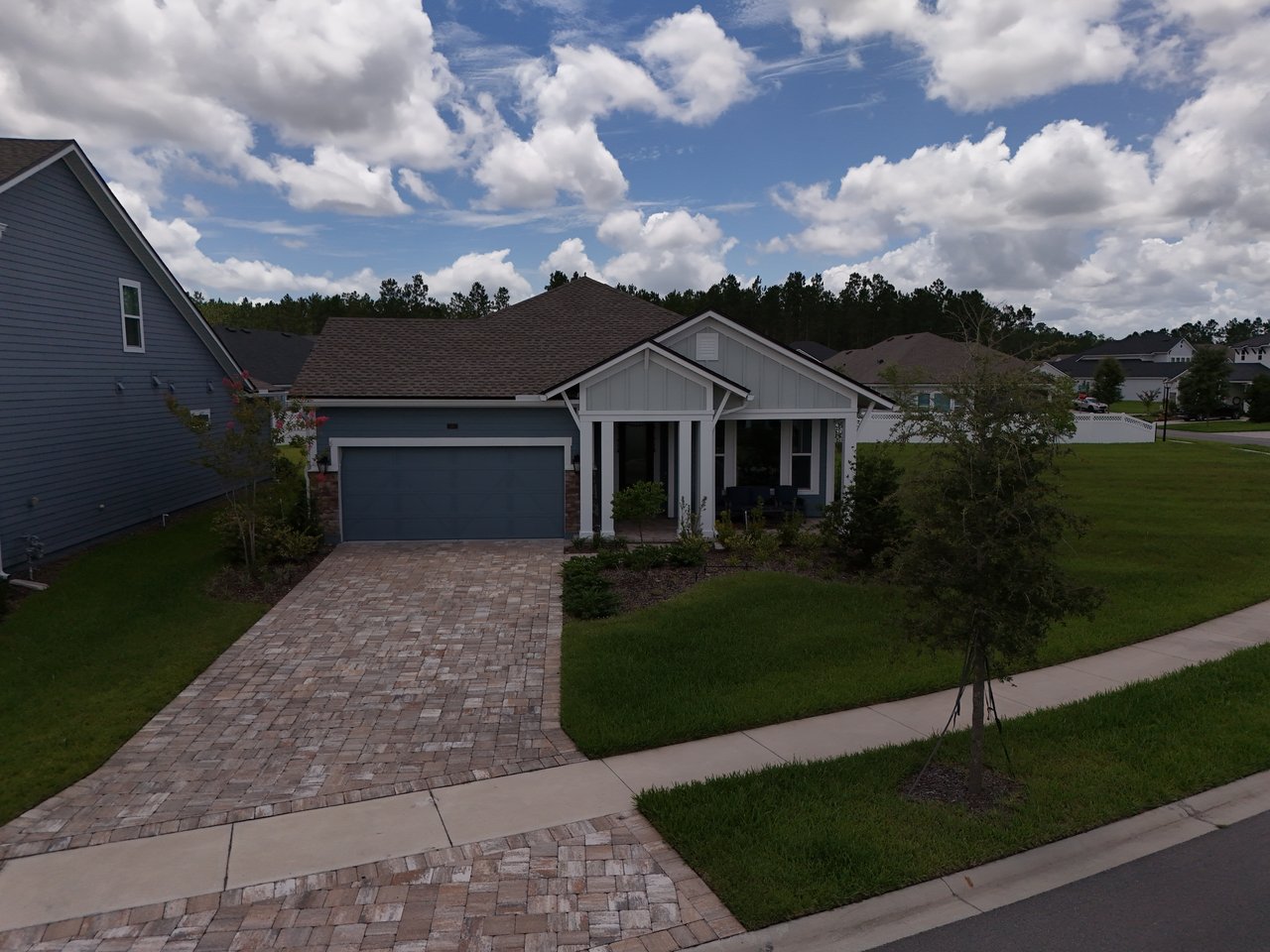Single-story blue-gray home with white trim, an attached garage, and a wide paver driveway.