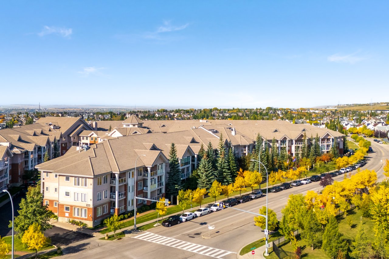 Condominium complex beside a broad road, viewed from above with yellow autumn trees.
