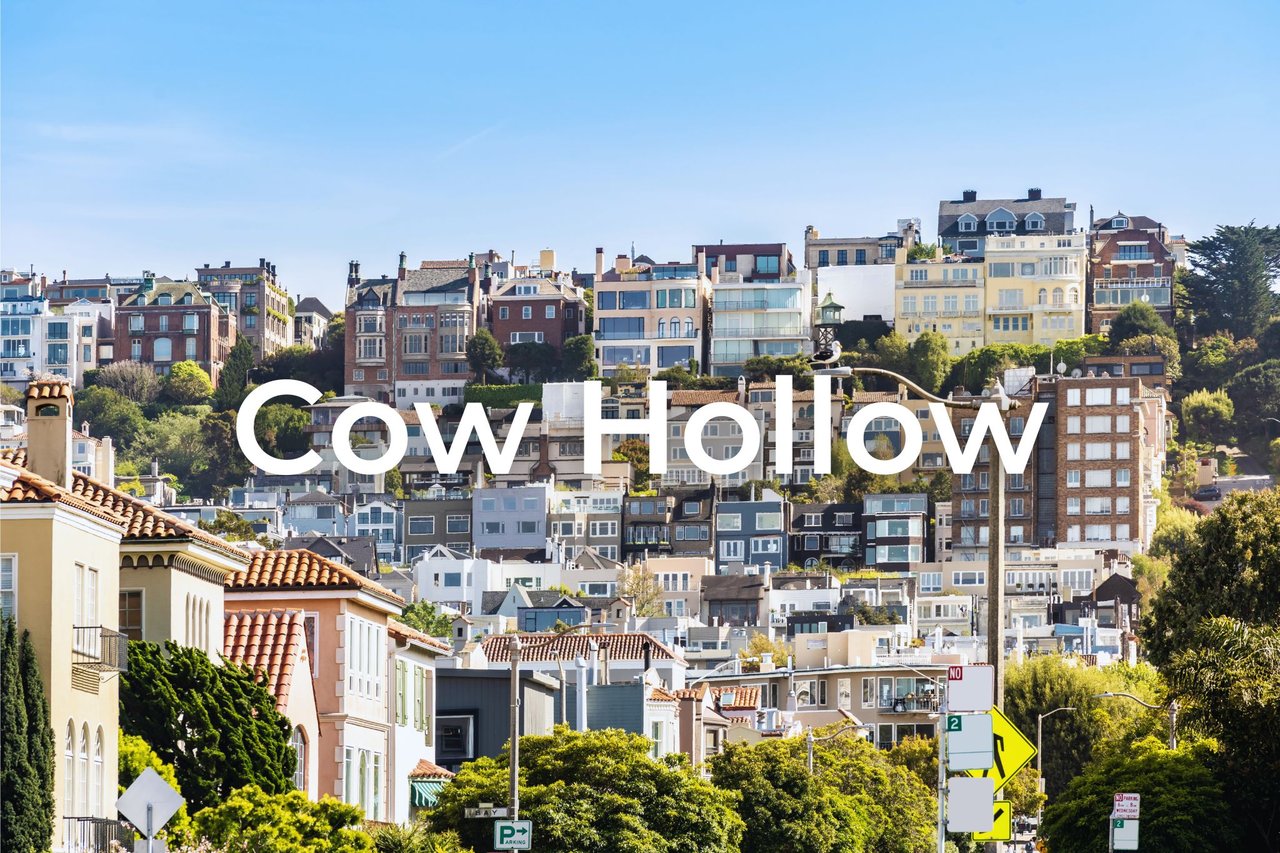 The image depicts a residential scene in the Cow Hollow neighborhood of San Francisco, featuring charming, upscale homes along a picturesque street. Overlaid text reads "Cow Hollow," highlighting this well-known, vibrant area known for its architectural beauty and community appeal.