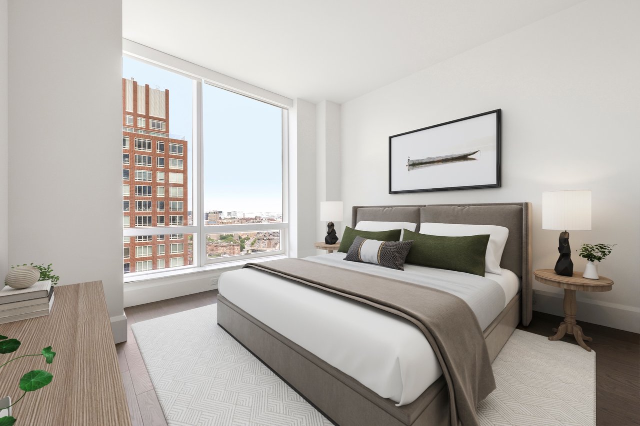 Staged bedroom with a large bed and floor-to-ceiling windows overlooking city buildings.