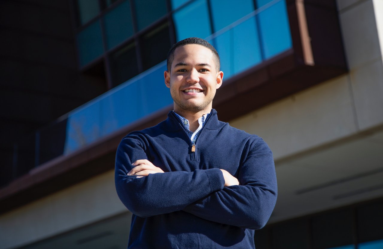 A. J. Graham smiles with his arms crossed in front of a modern glass building.