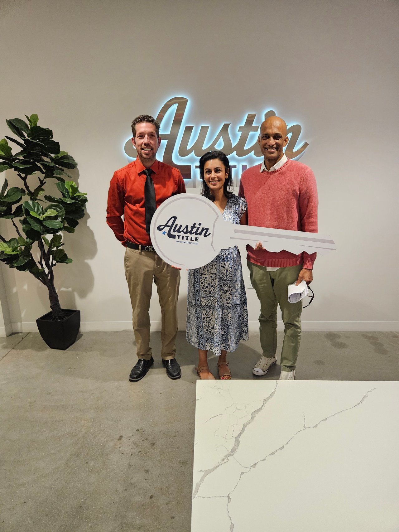Three adults pose with an oversized Austin Title key in front of an Austin sign.
