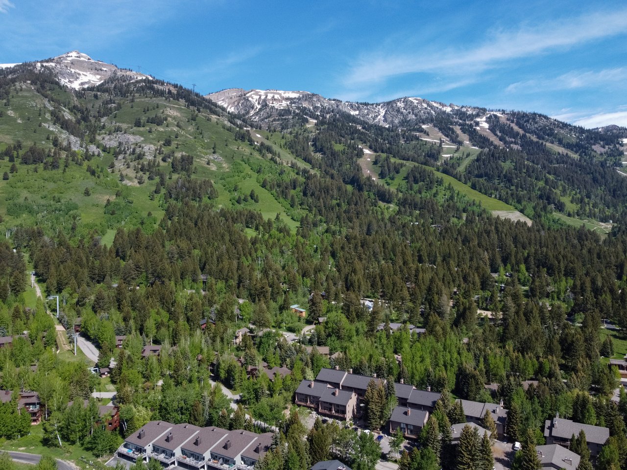 Aerial view of homes beneath a forested mountain ridge with patches of snow.
