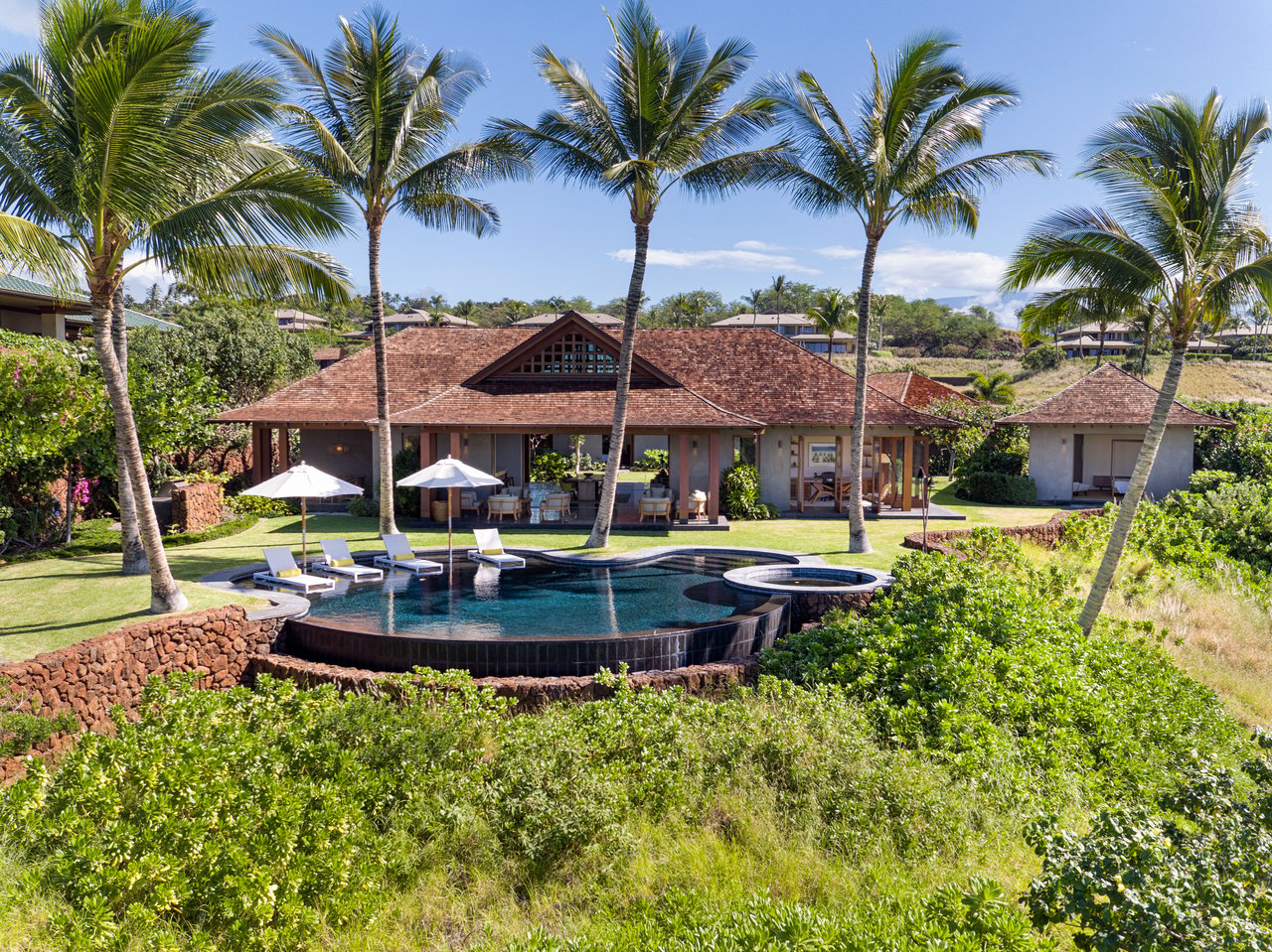 Tropical home with a covered lanai, palm trees, and a curved pool with a circular spa.