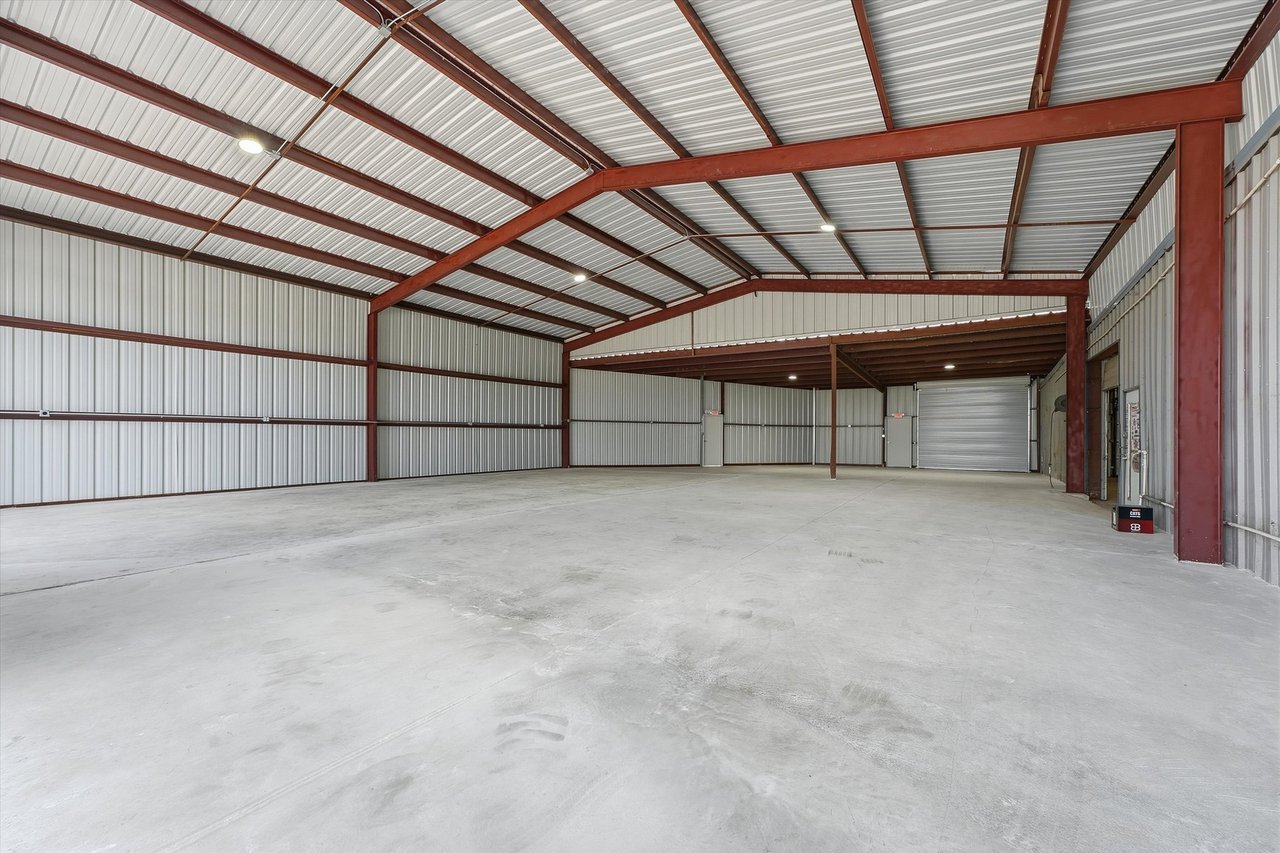 Empty metal outbuilding with red steel beams, a concrete floor, and a roll-up door.