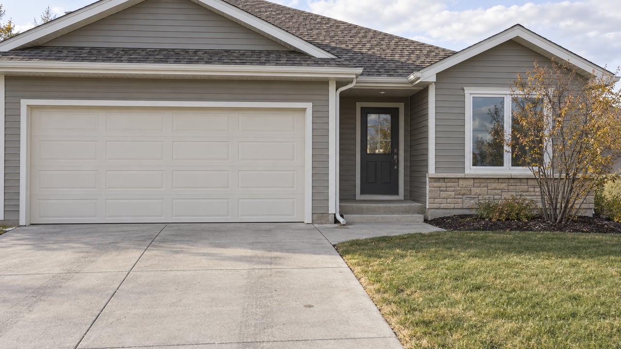 Gray-sided single-story home with a double garage, recessed entrance, concrete driveway and an autumn serviceberry beside the lawn.