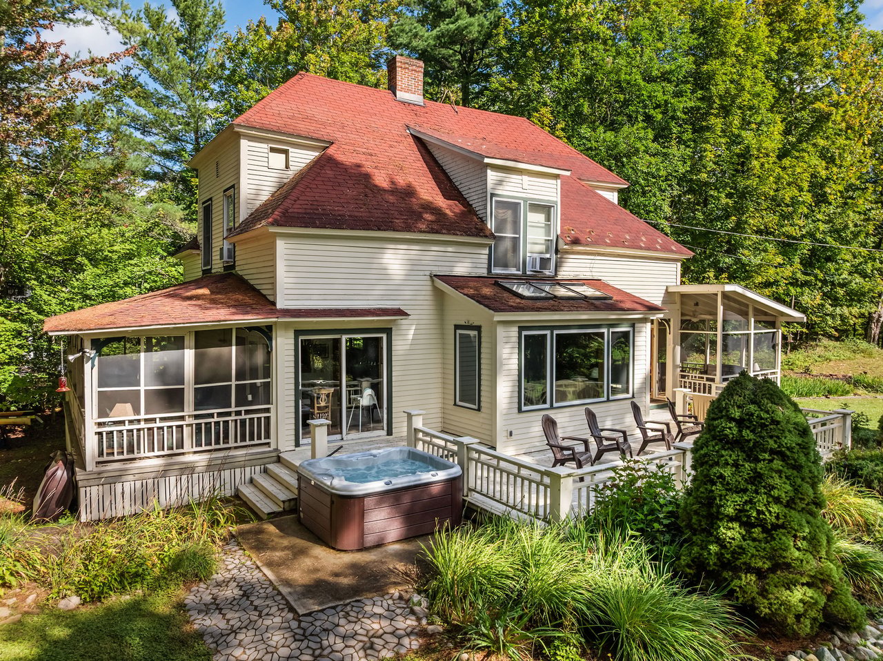 Wooded home with red roof, screened porch, deck seating, and a hot tub.
