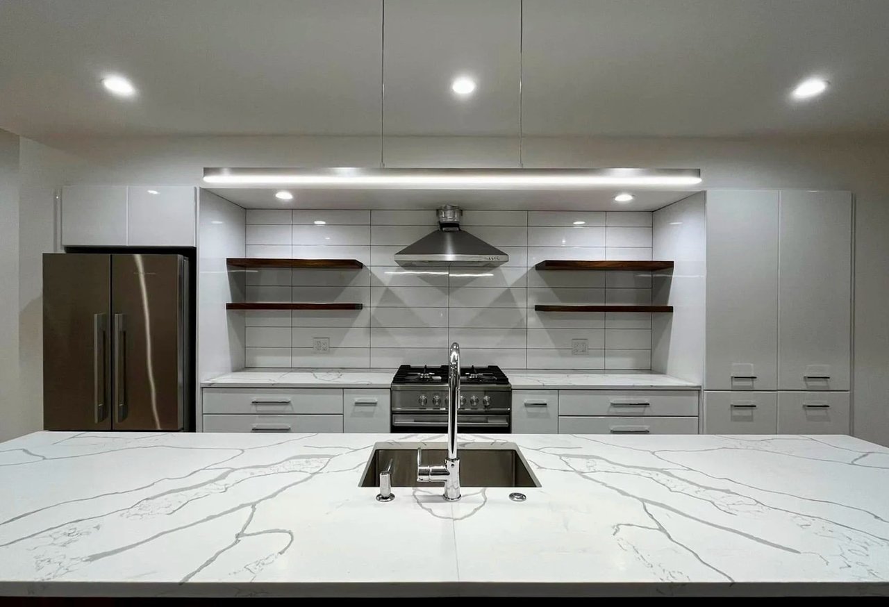 Modern kitchen with white cabinets and a veined stone island featuring an undermount sink.