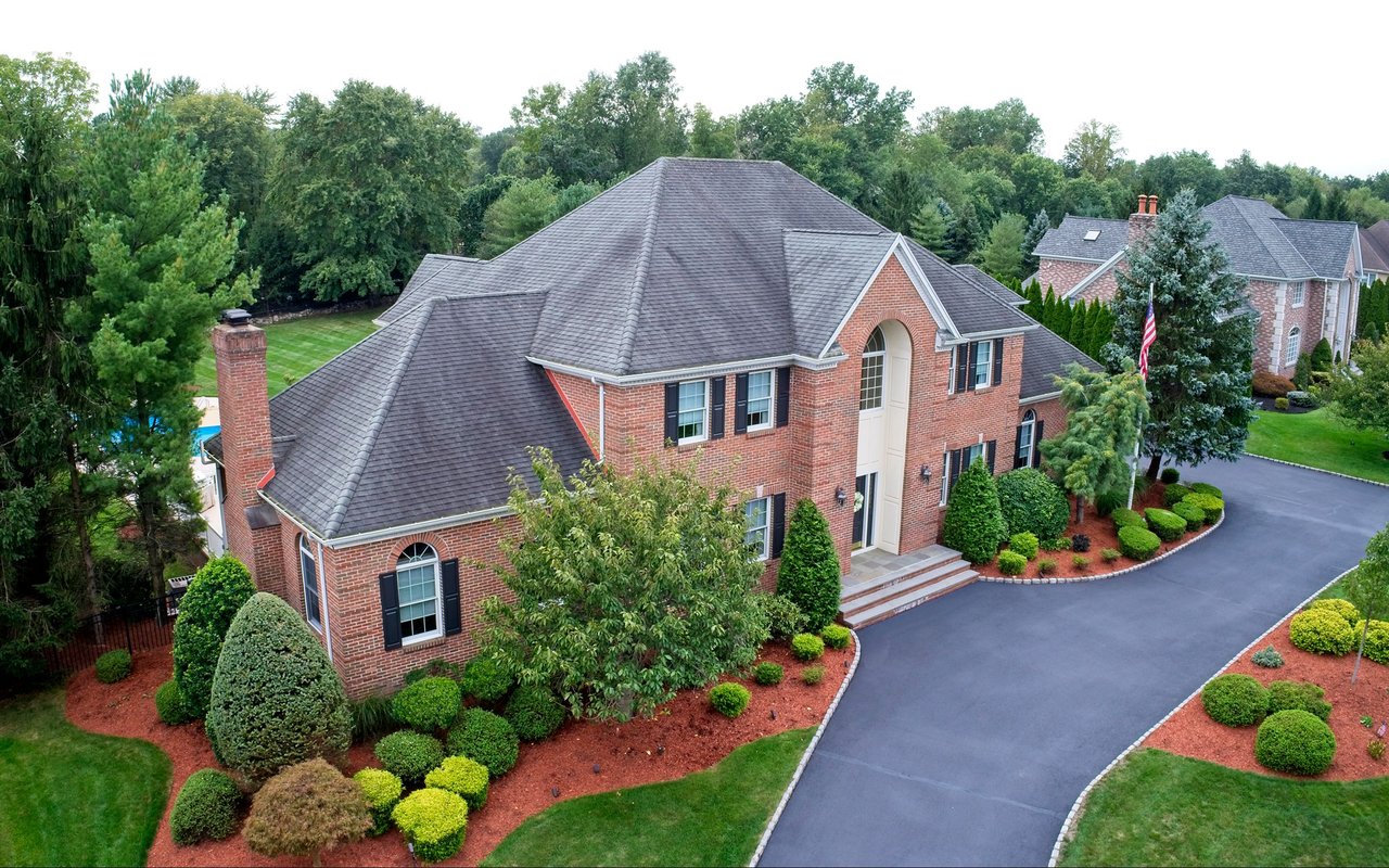 Aerial view of a red brick house with a gray roof, landscaped gardens, and a curved driveway.