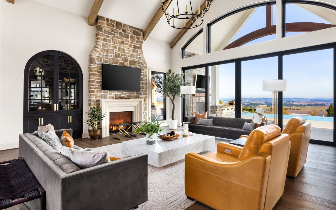 A cozy living room with a stone fireplace, furniture in various textures, and a pool view from floor-to-ceiling windows.