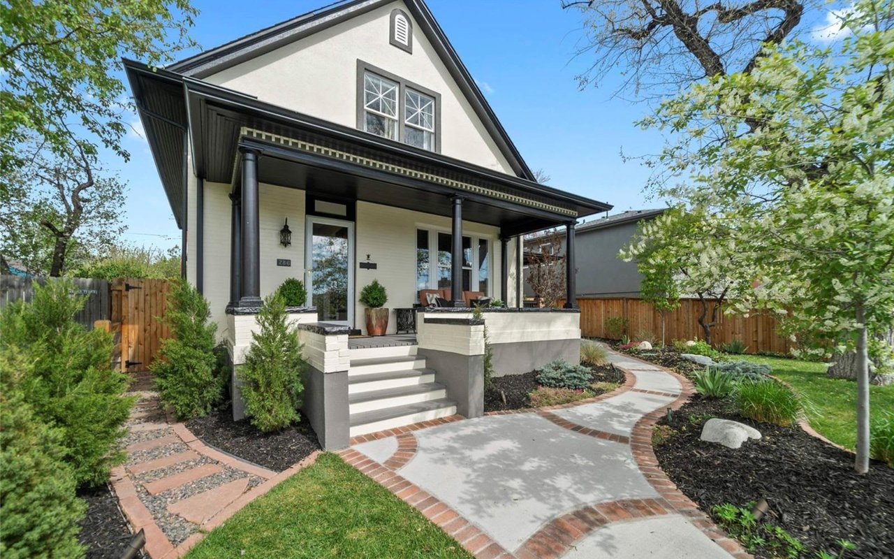  A charming two-story house with a light-colored stucco exterior and dark trim, featuring a welcoming front porch.