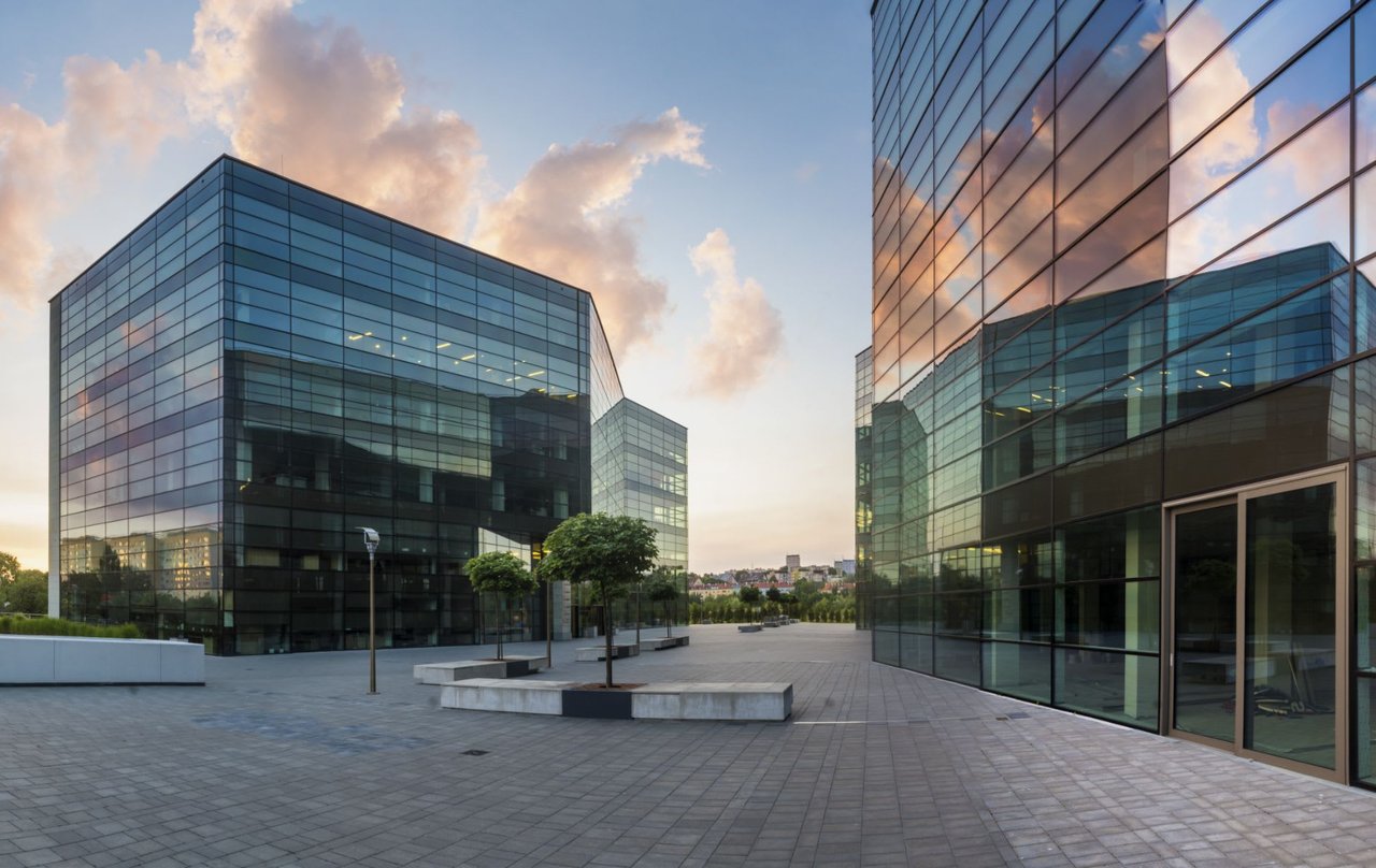 A panoramic view of two office buildings with large glass windows reflecting the golden light of the setting sun.